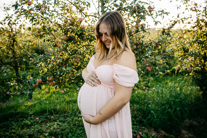 schwangere Frau im Kleid steht vor Apfelbaum